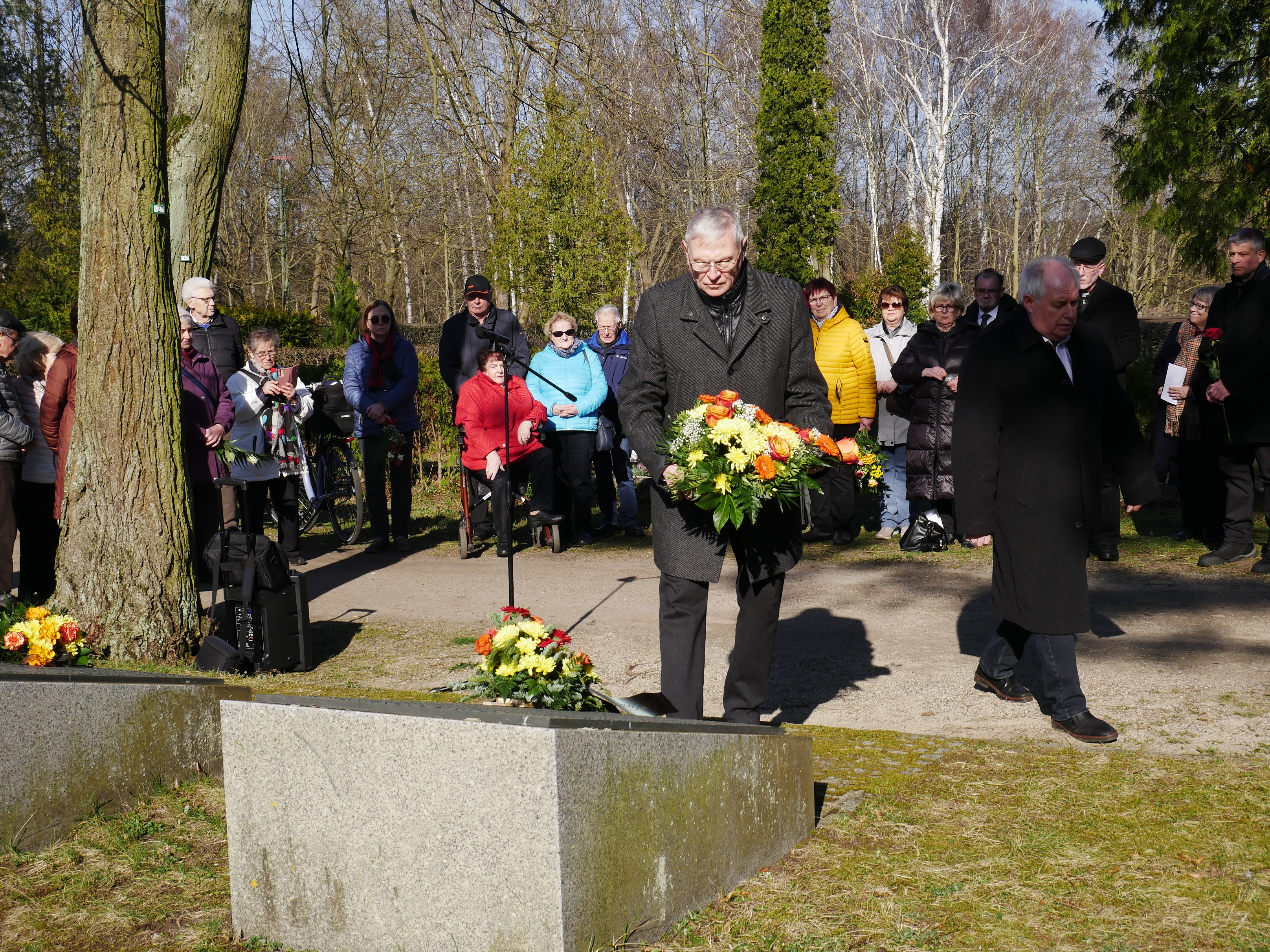 Lothar Eysser, der Vorsitzende der Stadtverordnetenversammlung Erkner, legt ein Gebinde am Gräberfeld auf dem Friedhofwährend der ersten Kranzniederlegung ab.