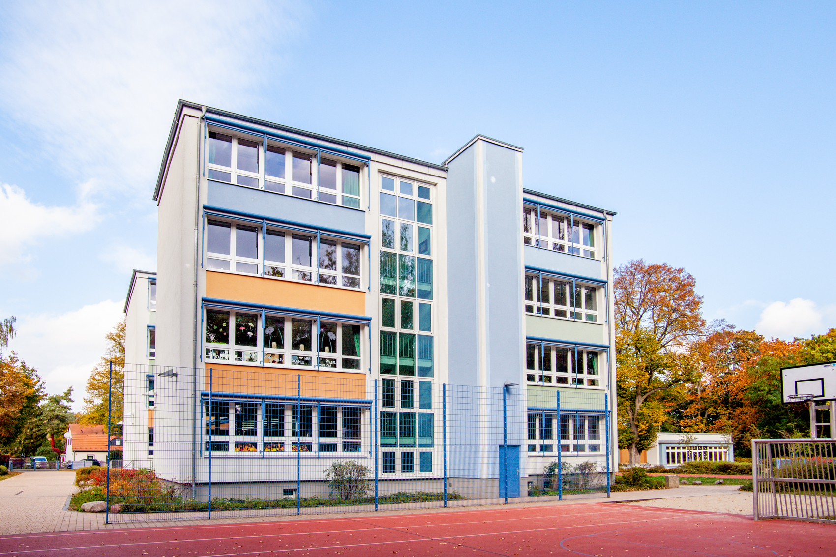 vierstöckiges Schulgebäude mit farbigen Akzenten und Ballspielfeld
