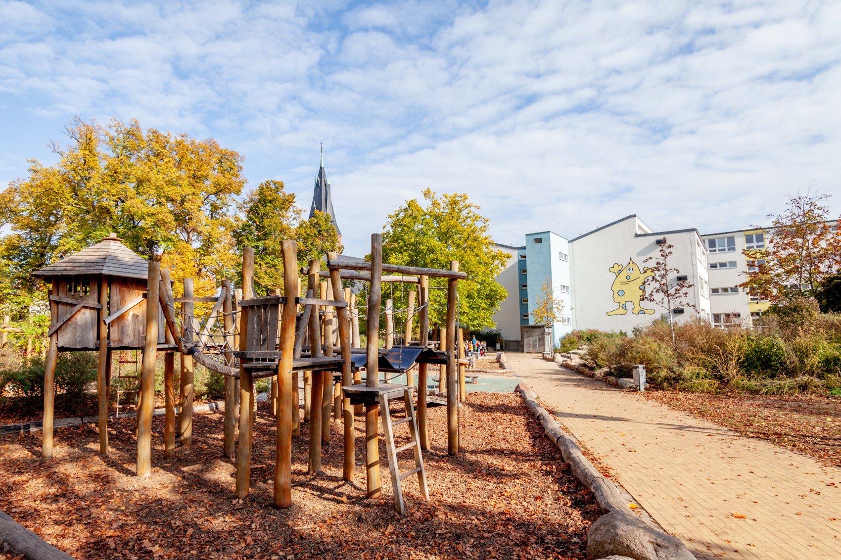 Spielgeräte aus Naturstämmen mit Schulgebäude im Hintergrund