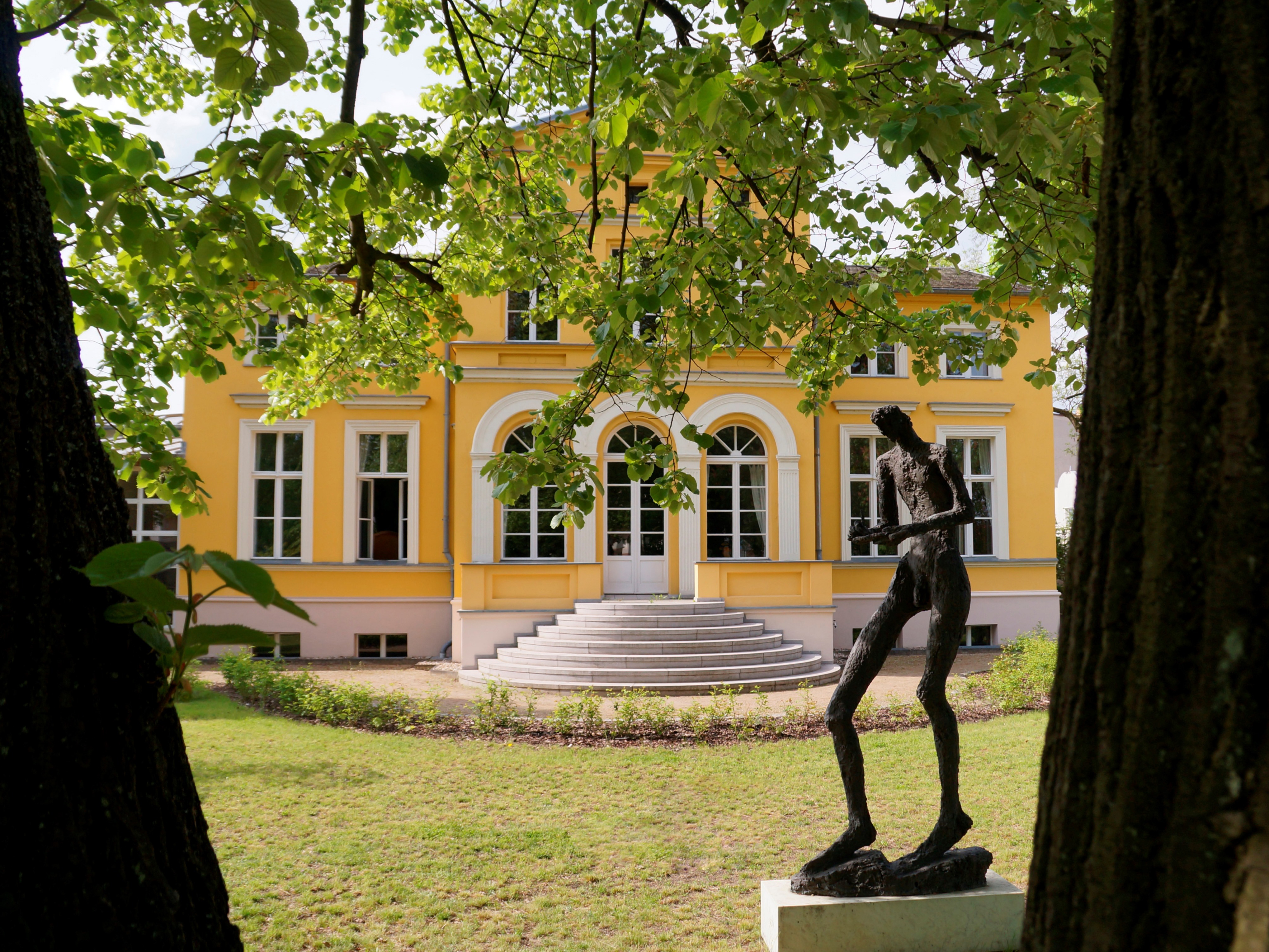 Farbenfrohe gelbe Villa Lassen von Bäumen eingerahmt mit Skulptur und